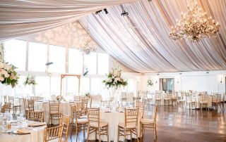 A wedding reception in a large room with white drapes and chandeliers.