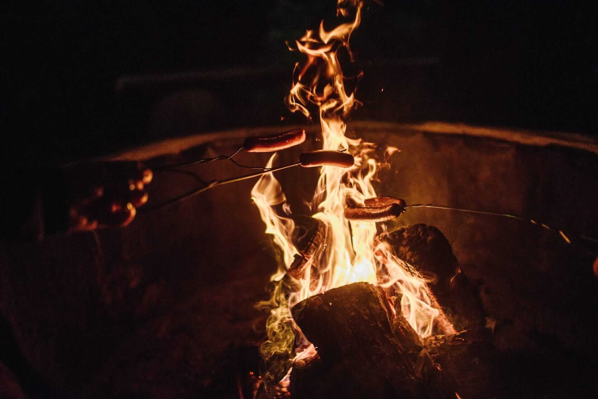 A person is cooking hotdogs over a campfire during a wedding experience.