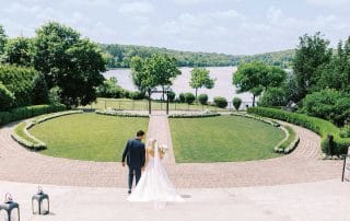 A bride and groom walking down a path in front of a lake.