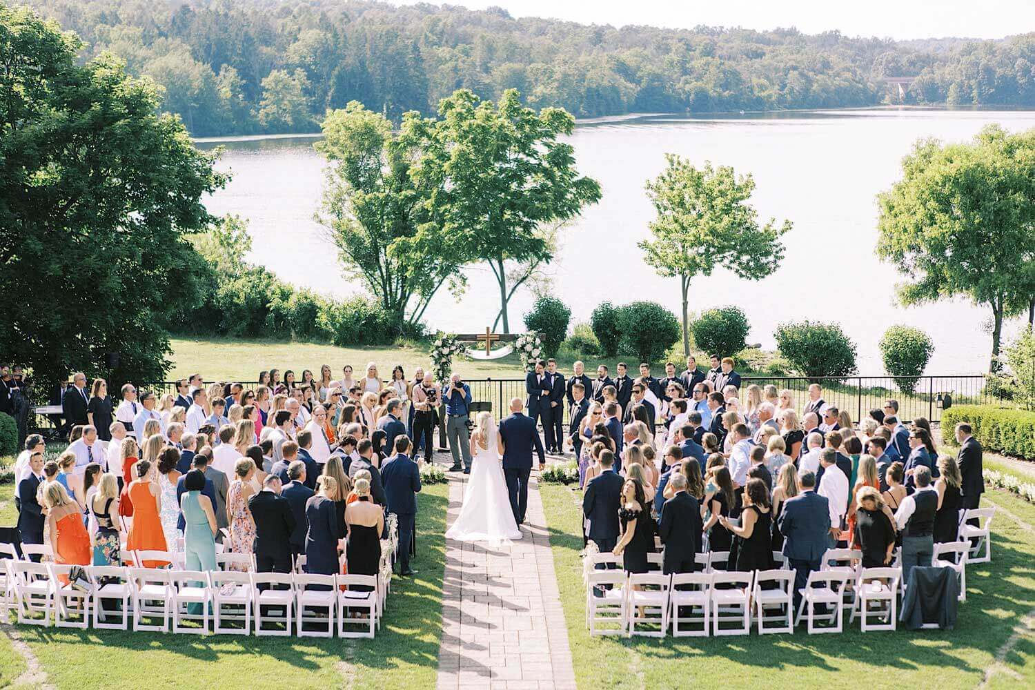 Lake-House-Inn-Wedding-0069-two17photo A wedding ceremony on a grassy lawn with a lake in the background.